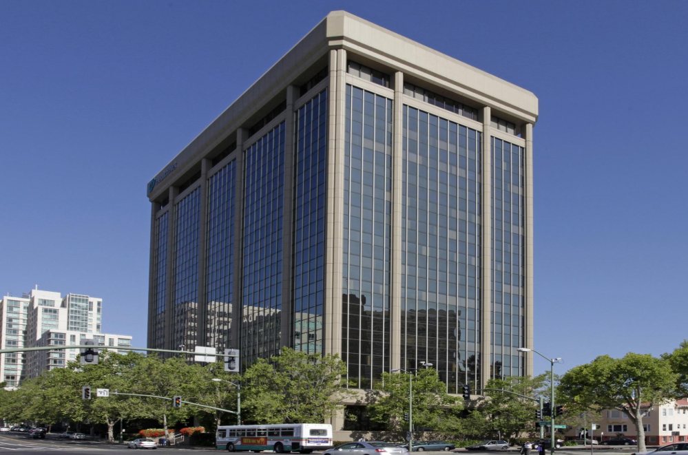 Grand Avenue office tower: a tall building with vertical stone columns framing dark glass windows, rising above street trees against a clear blue sky.